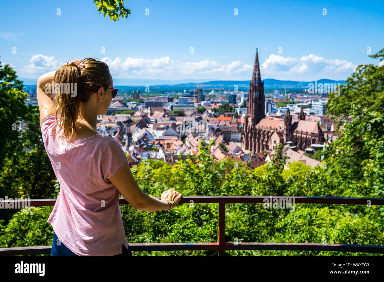 Germania, incredibili giovane donna in piedi sopra la città di Freiburg im Breisgau città vecchia e la famosa cattedrale minster in estate Foto Stock