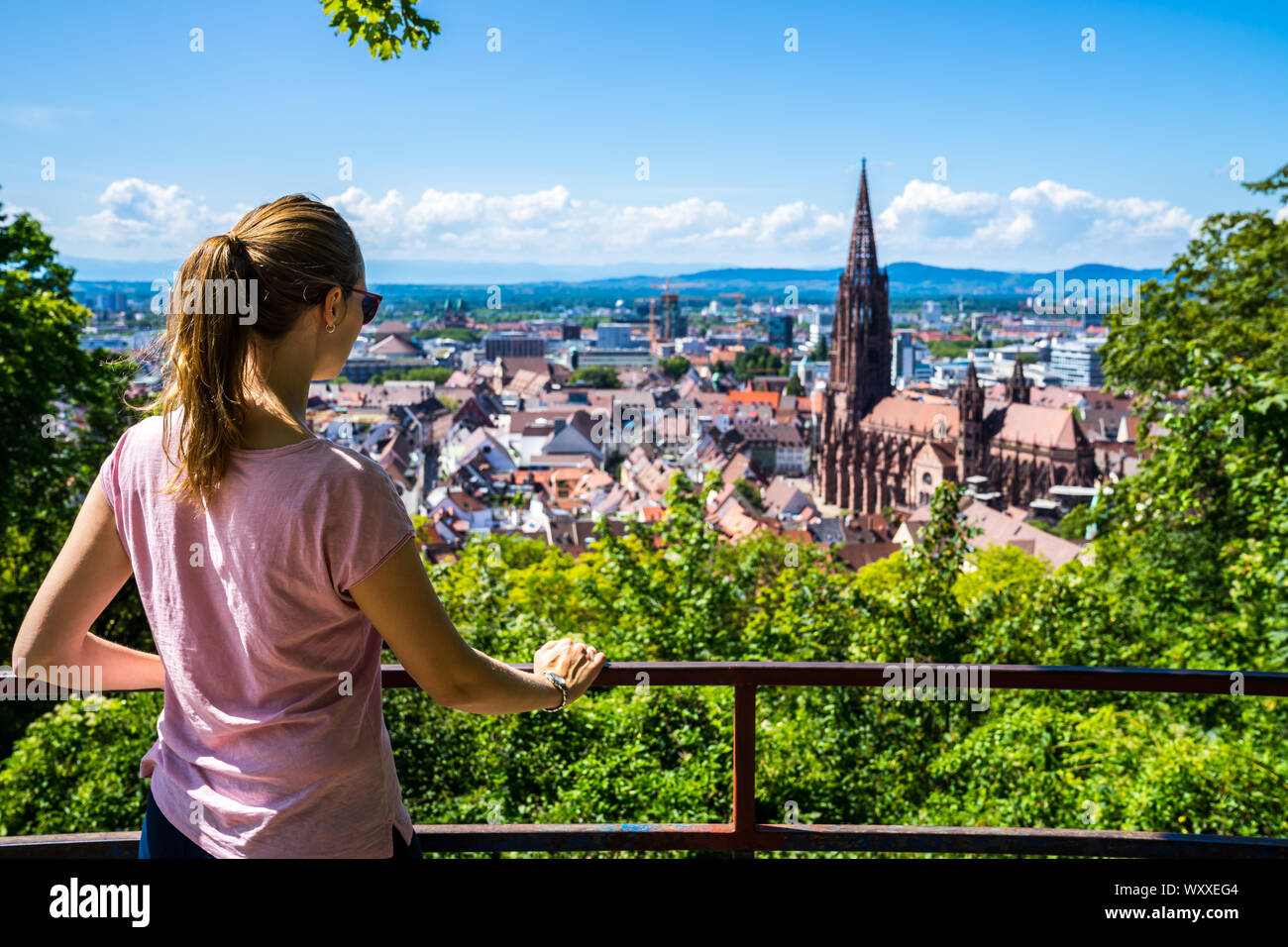 Germania, giovane e bella ragazza turistica sovrastante skyline di Freiburg im Breisgau city e la famosa cattedrale di Muenster in estate circondato dal verde Foto Stock