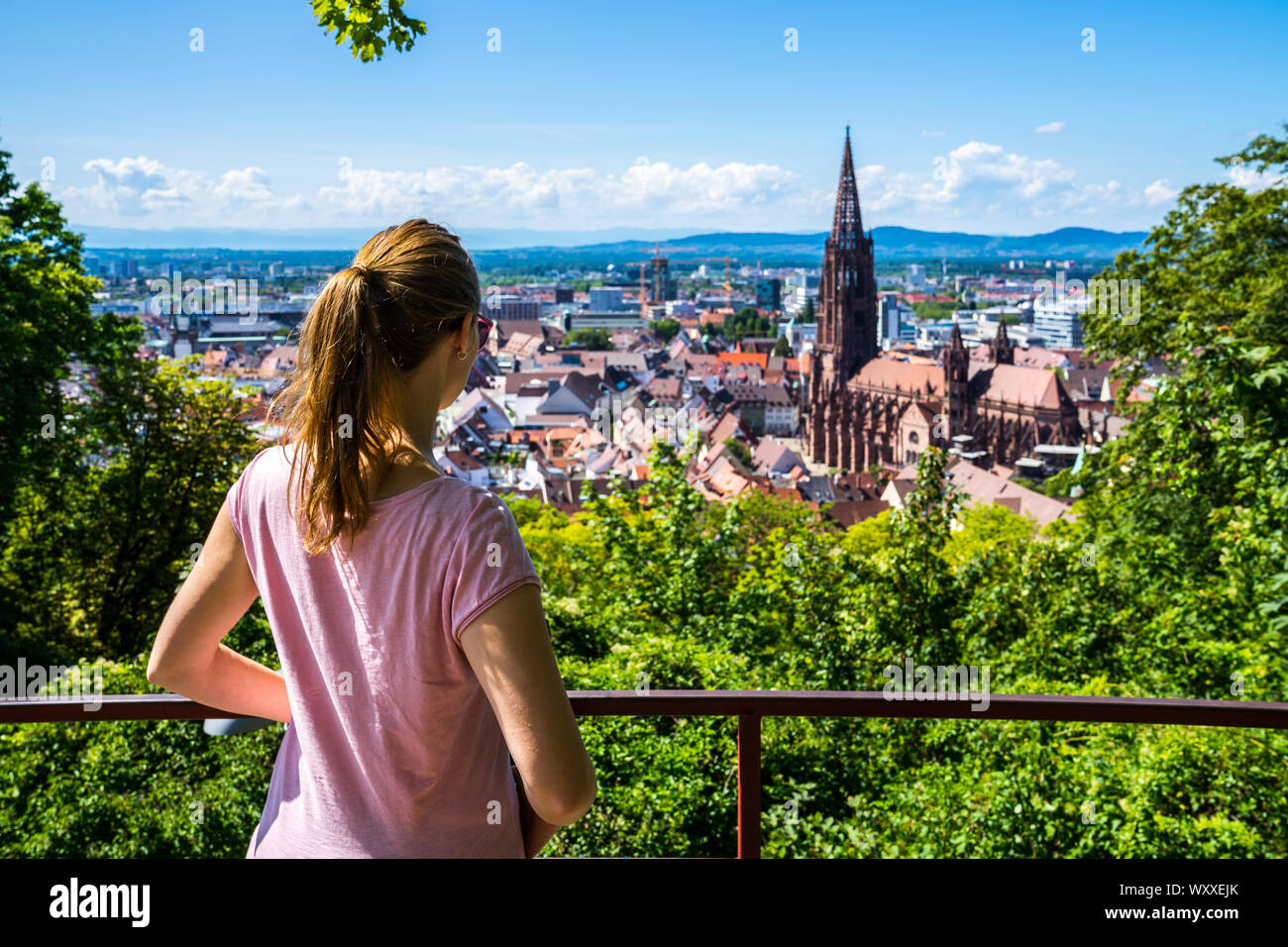Germania, incredibile donna bionda con la coda di cavallo godendo di vista al di sopra città Freiburg im Breisgau e sullo skyline con la famosa cattedrale di Muenster in estate vacati Foto Stock