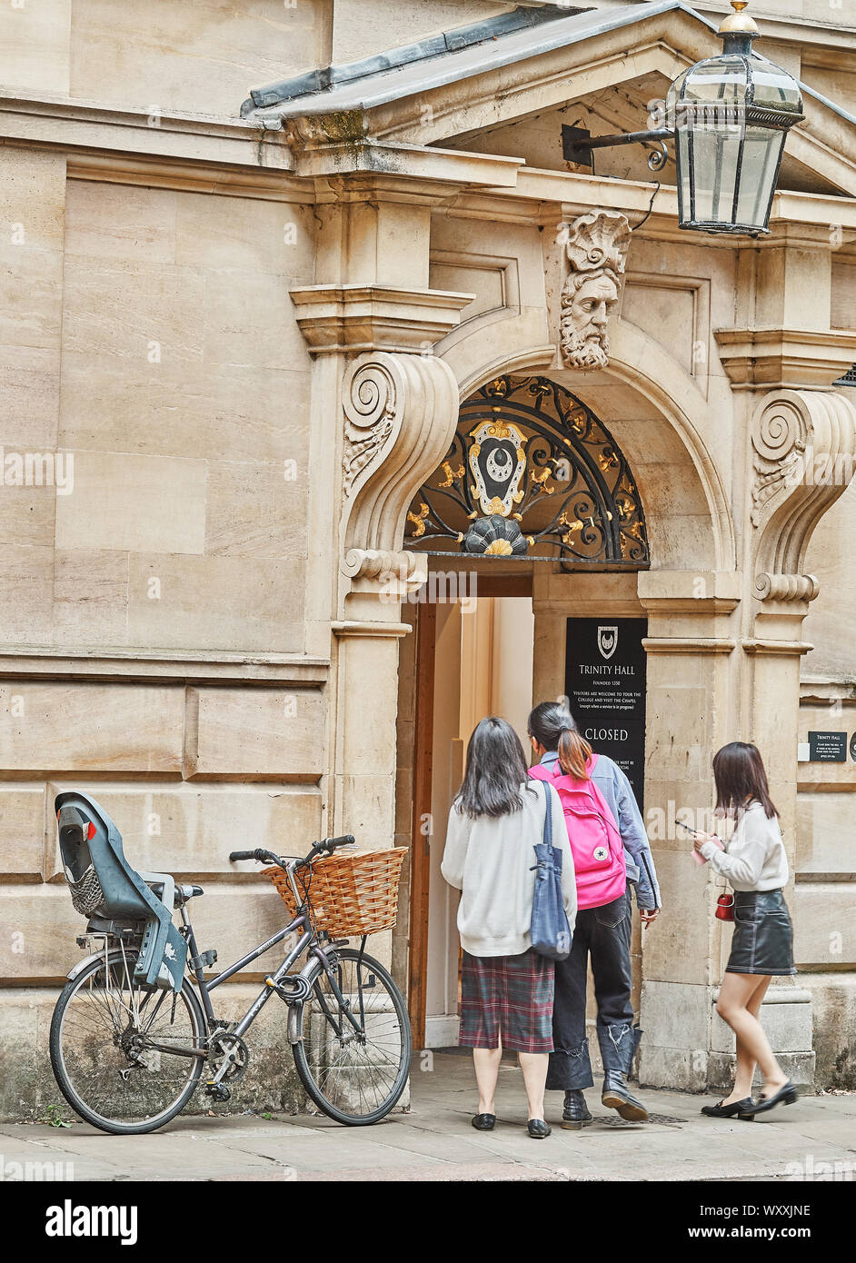 Un trio femminile di turisti guardano con cautela nell'ingresso della Trinità Hall dell'università di Cambridge, Inghilterra. Foto Stock