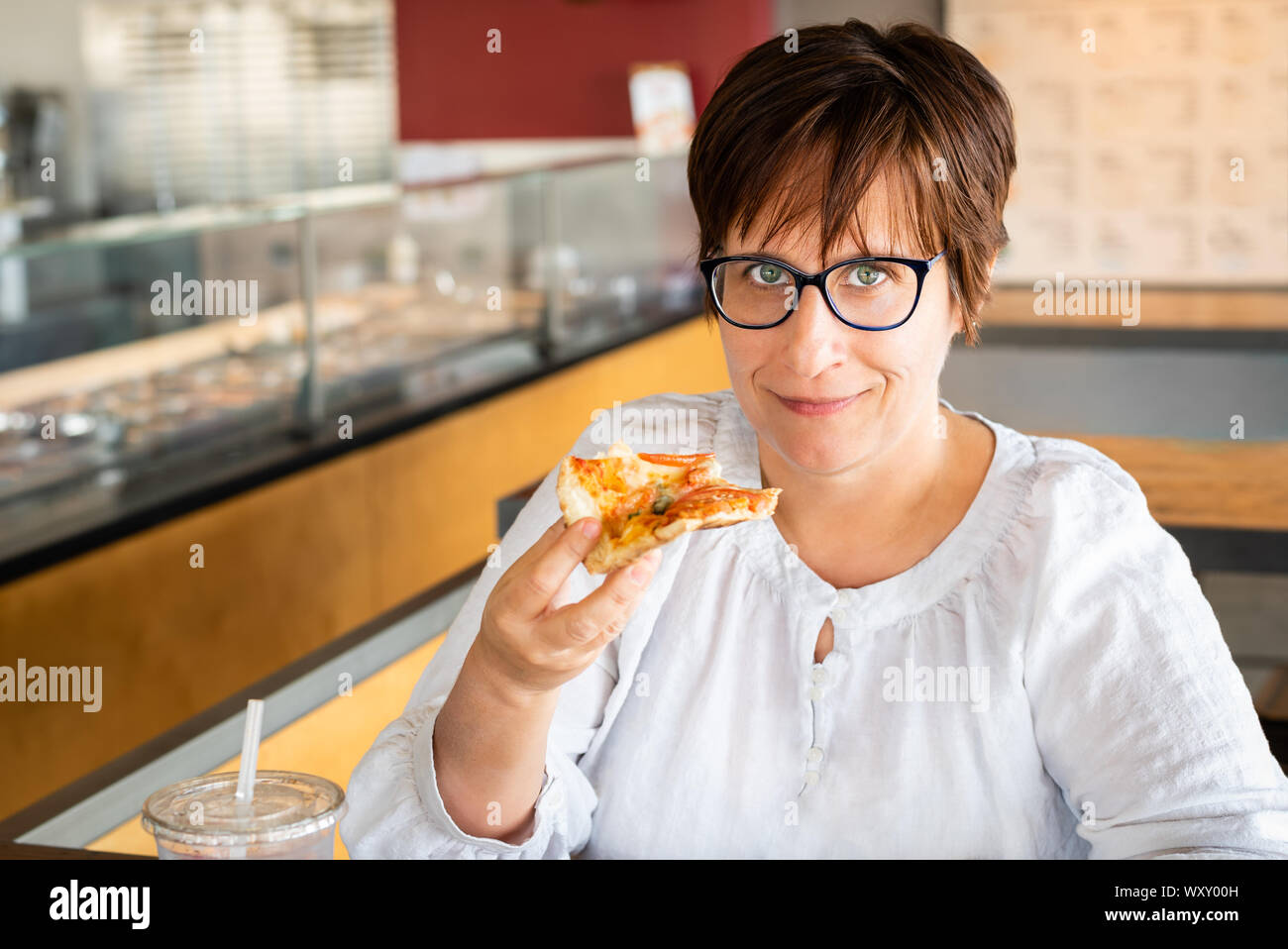 La donna caucasica con occhi verdi, capelli corti e occhiali di mangiare la pizza in un ristorante. Foto Stock