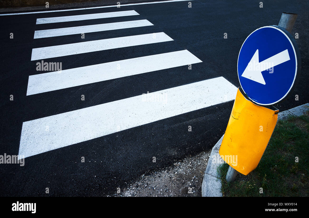 Un cartello blu con una freccia bianca indica strisce per un attraversamento pedonale sull'asfalto di una strada di città Foto Stock