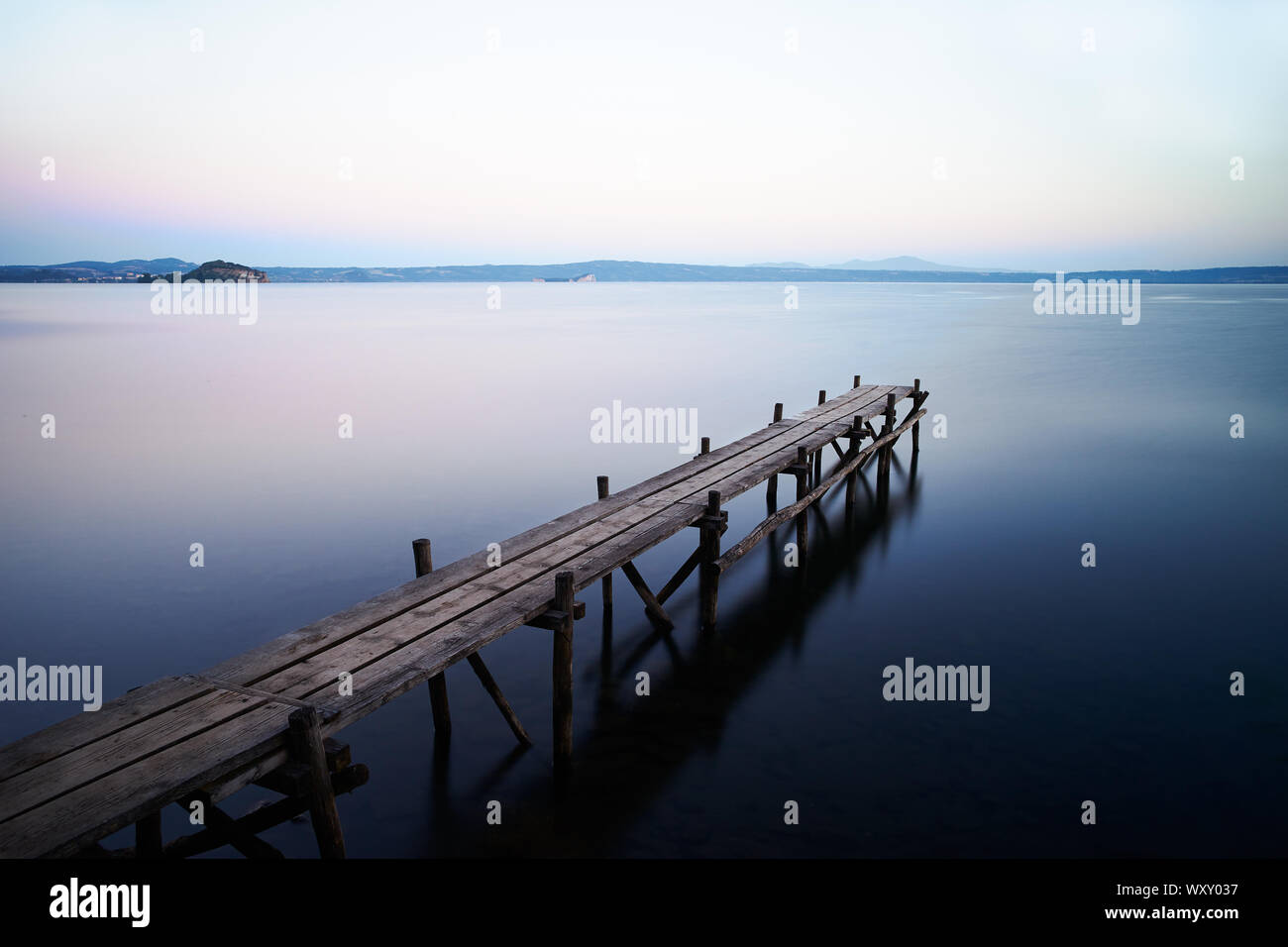 Una lunga esposizione di un paesaggio con un vecchio molo in legno sulle acque del lago di Bolsena Foto Stock