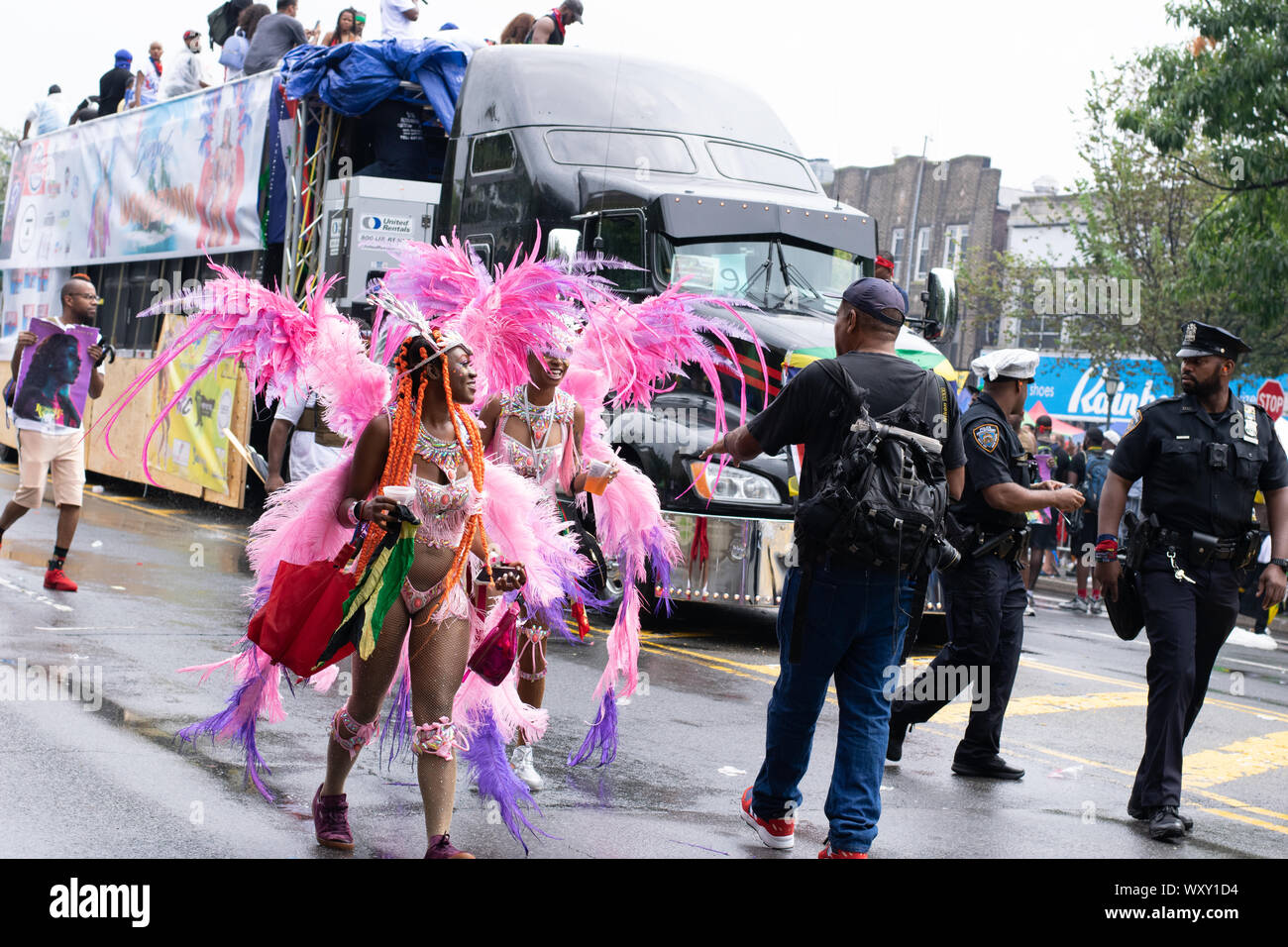 Tanzend zu lauter Musik laufen zwei Frauen mit rosafarbenem Kostüm und Federn auf der West Indian Day Parade di New York City Un den Zuschauern vorbei Foto Stock