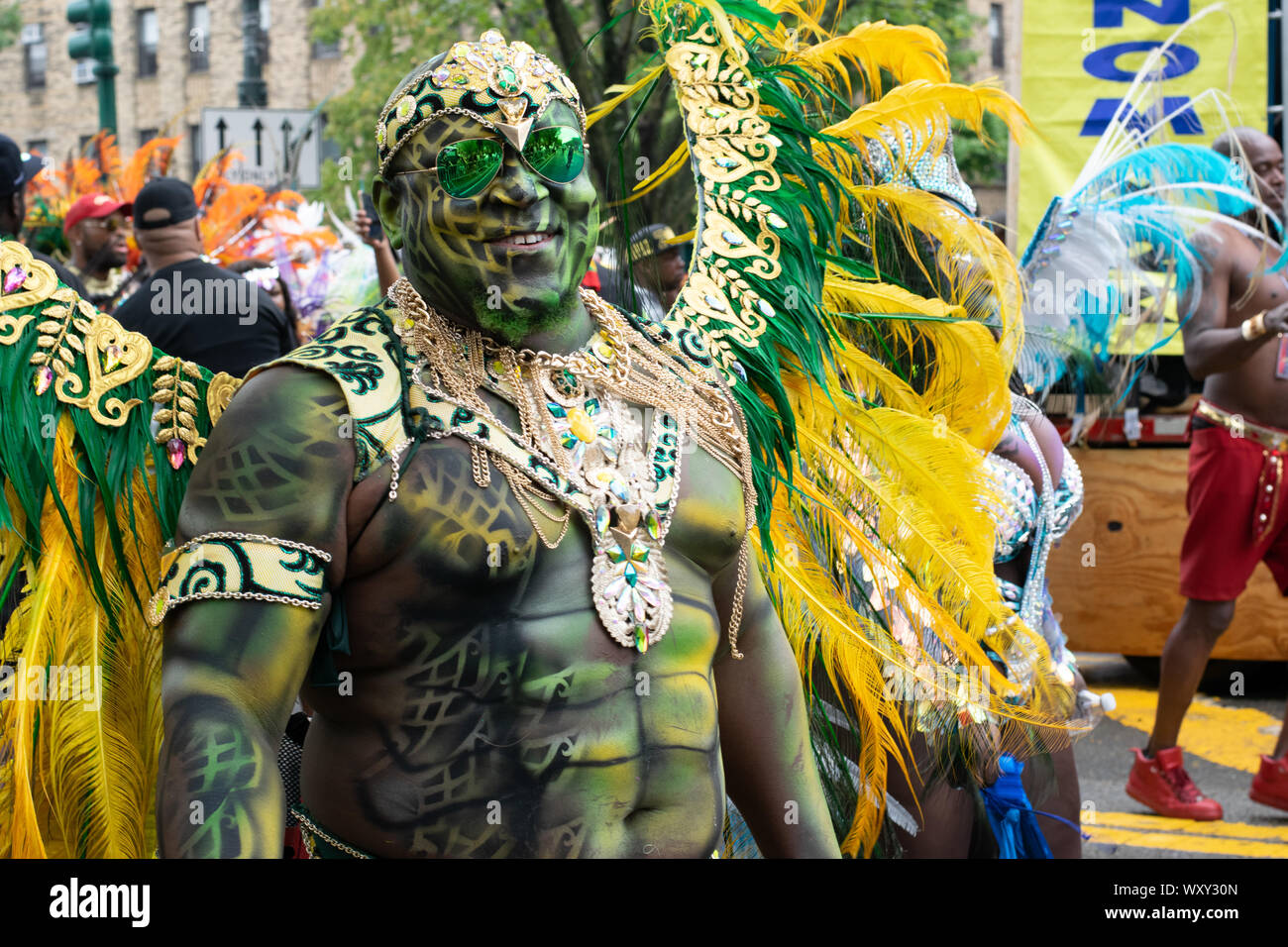 Stolz auf seine Körperbemalung blickt ein Teilnehmer der West Indian Day Parade di New York City in die Kamera. Auf dem Rücken trägt er Federschmuck. Foto Stock