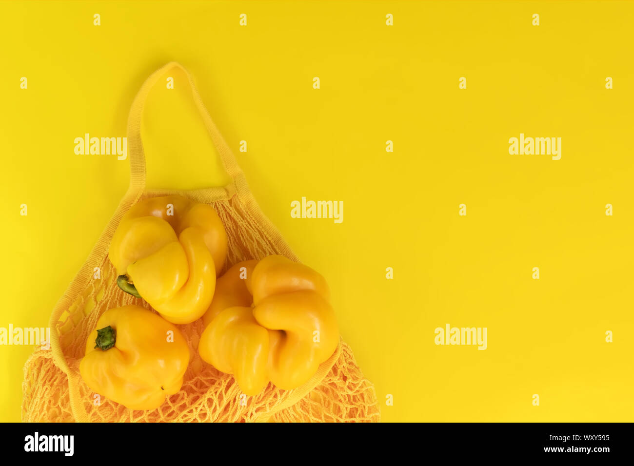 Stringa di giallo borsa con Giallo peperoni freschi su sfondo giallo. Eco Bio prodotti, brutto alimenti naturali, sana, dietetica e vegetariana alimenti. Consente di visualizzare Foto Stock