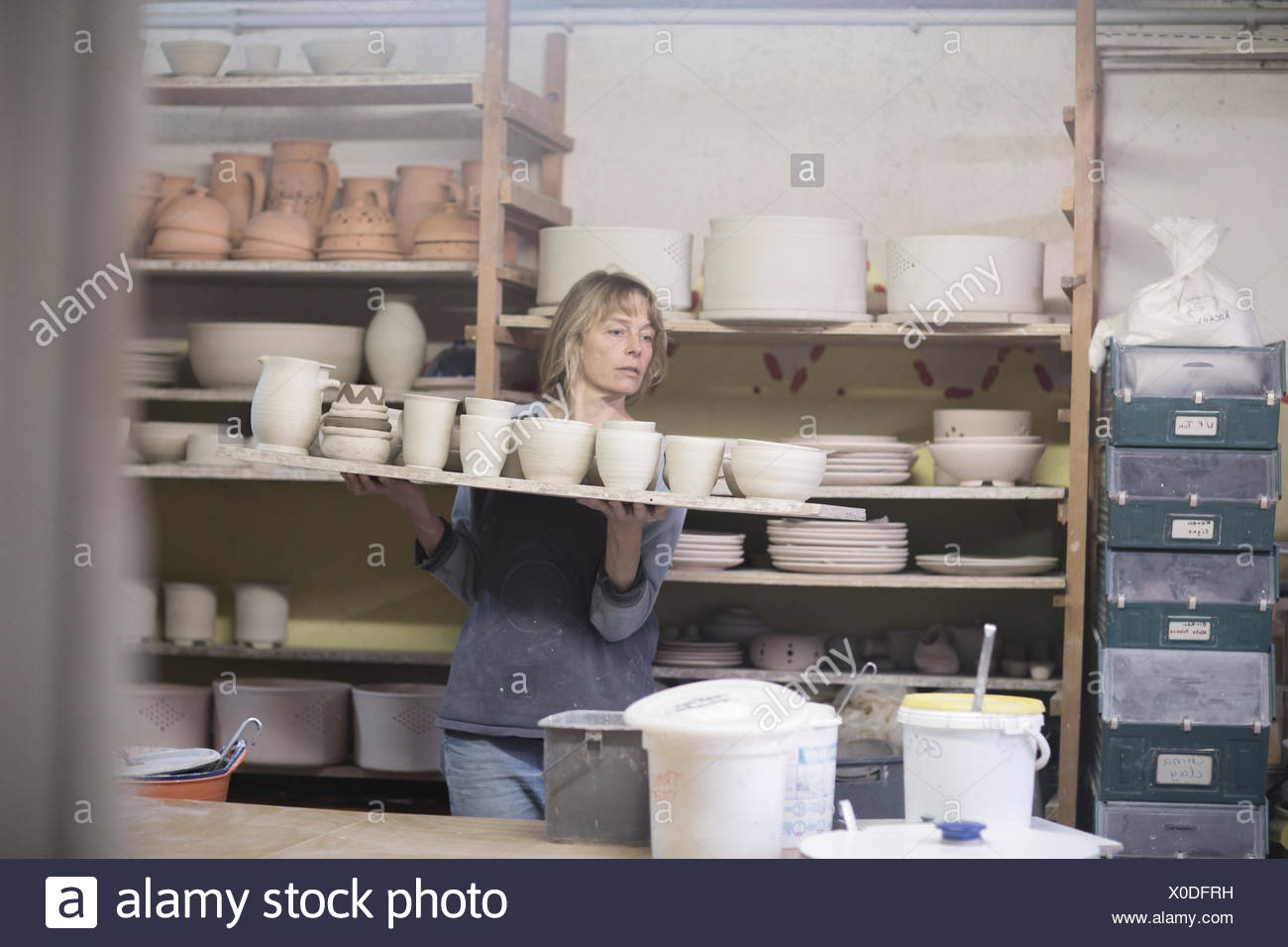 Potter femmina che porta il vassoio di vasi di terracotta in officina Foto Stock