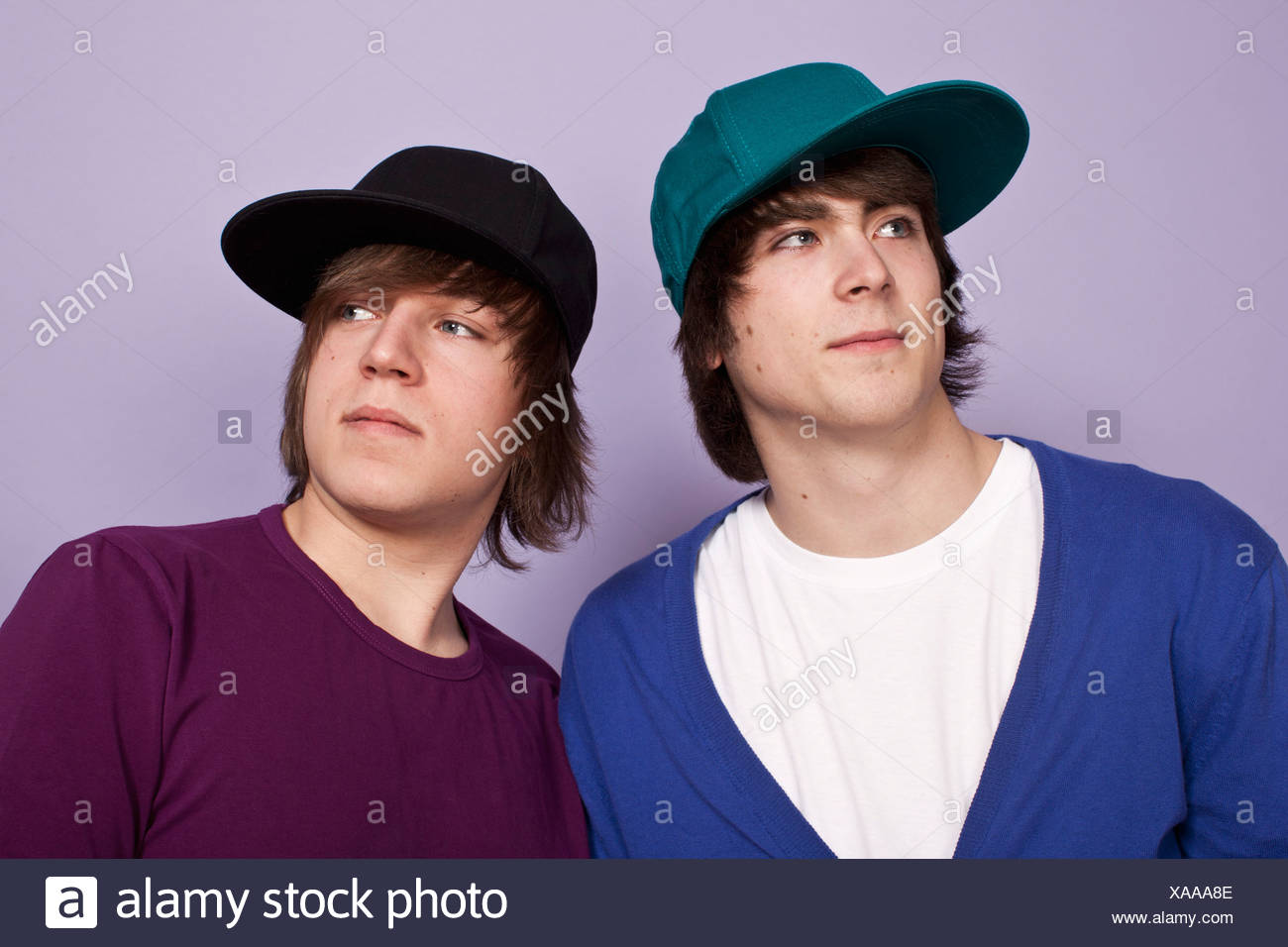 Due ragazzi adolescenti Indossando cappellini da baseball lo sguardo lontano, studio shot Foto Stock
