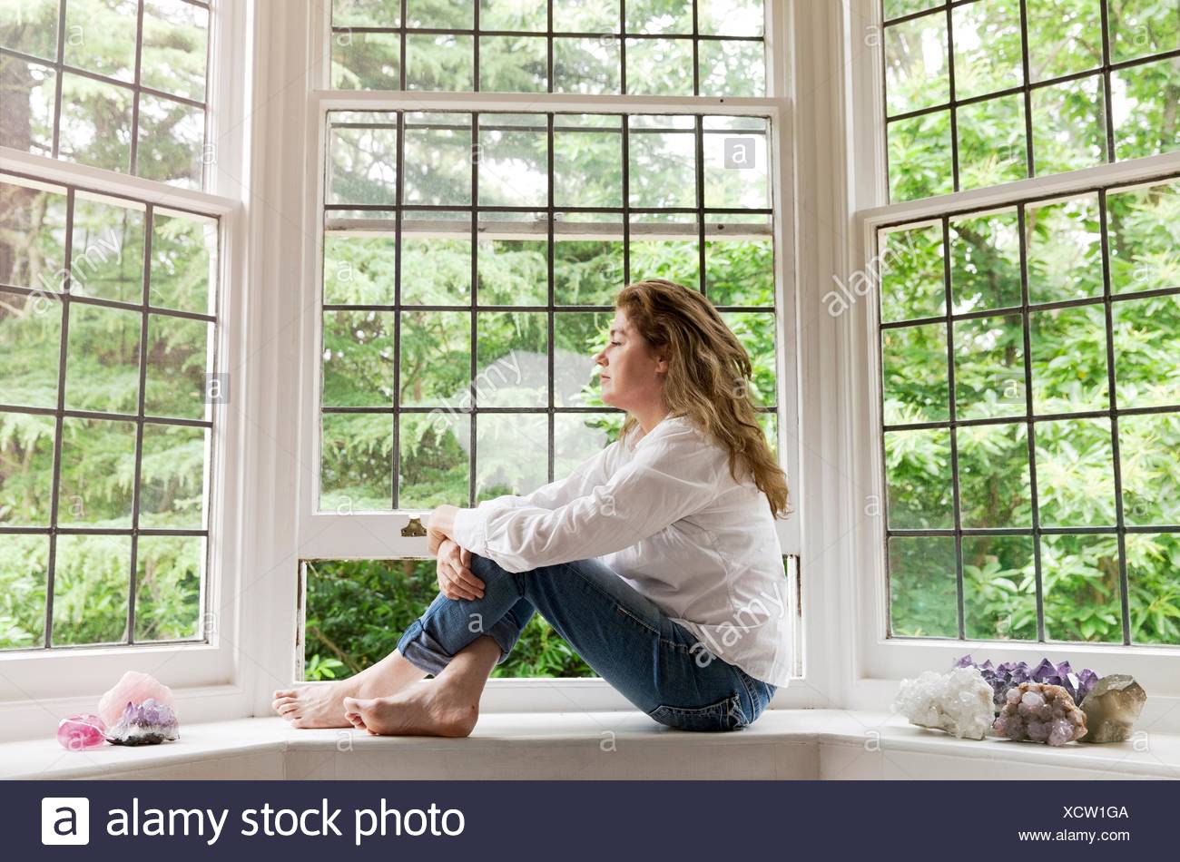 Ritratto di donna matura seduta sul soggiorno davanzale guardando fuori della finestra Foto Stock