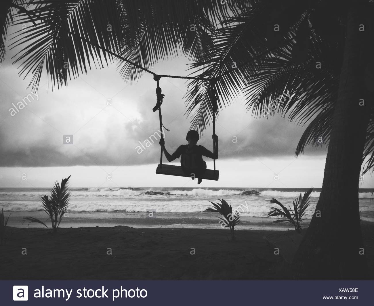 Silhouette of boy sitting on a swing on the beach